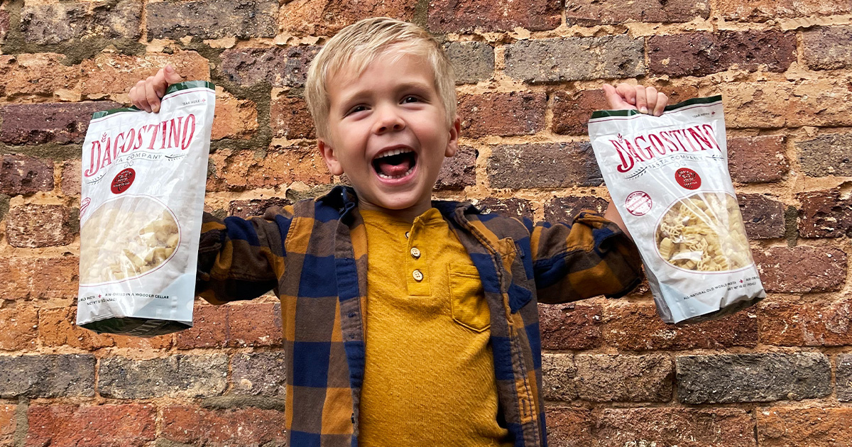 Young boy joyfully holding two bags of the redesigned Dagostino Pasta packaging, encapsulating the brand's essence.